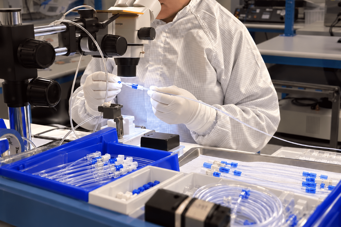 Medical device technician assembling catheter components under a microscope at Pathway MedTech